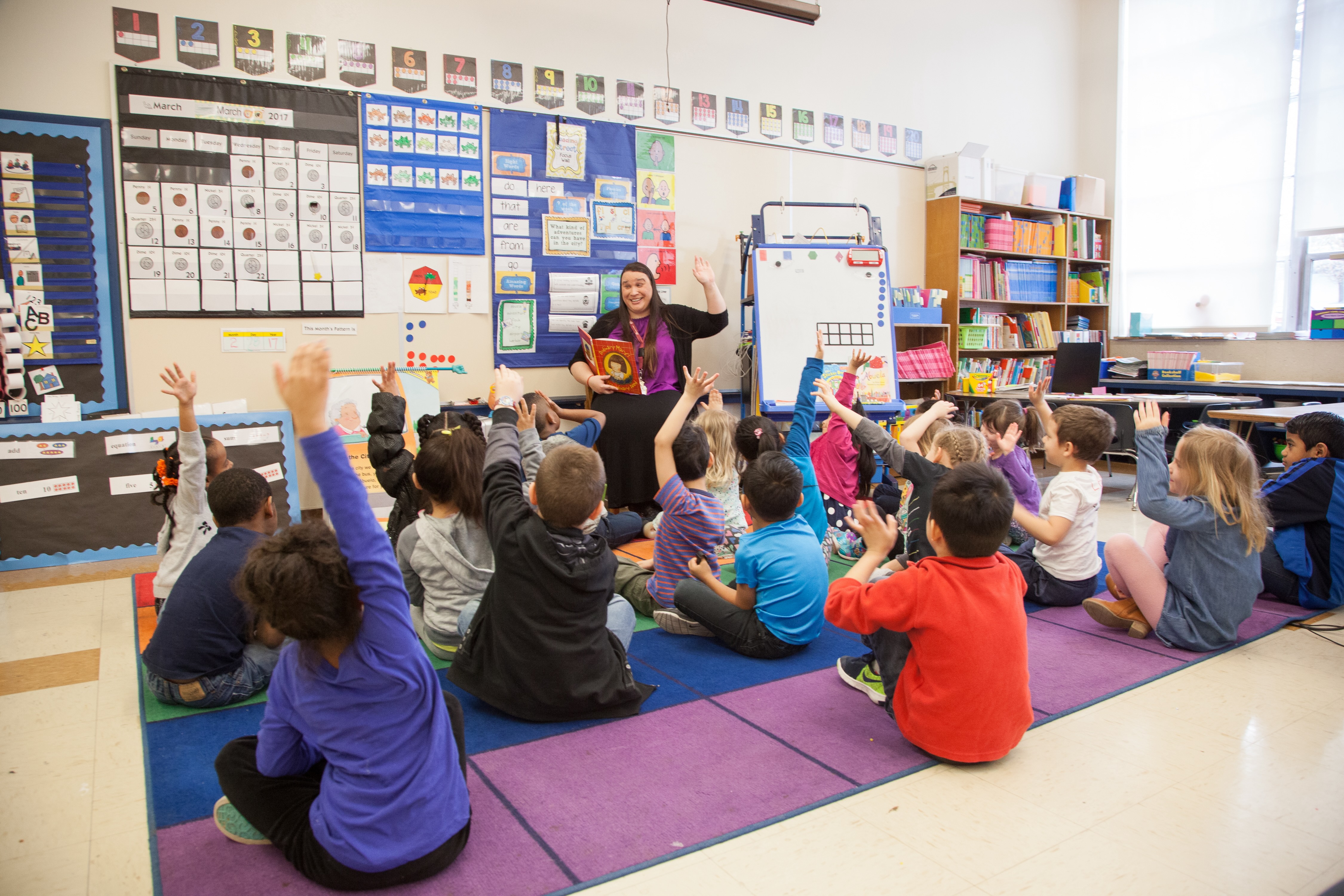 A classroom of children raising their hands